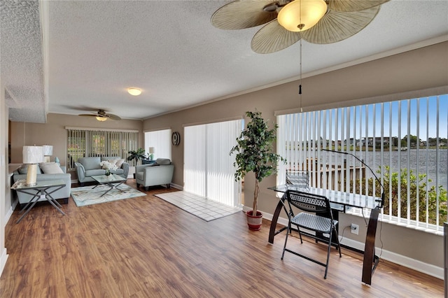 living area featuring a water view, a textured ceiling, baseboards, and wood finished floors