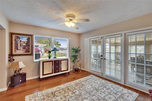 living area with a ceiling fan, a textured ceiling, baseboards, and wood finished floors