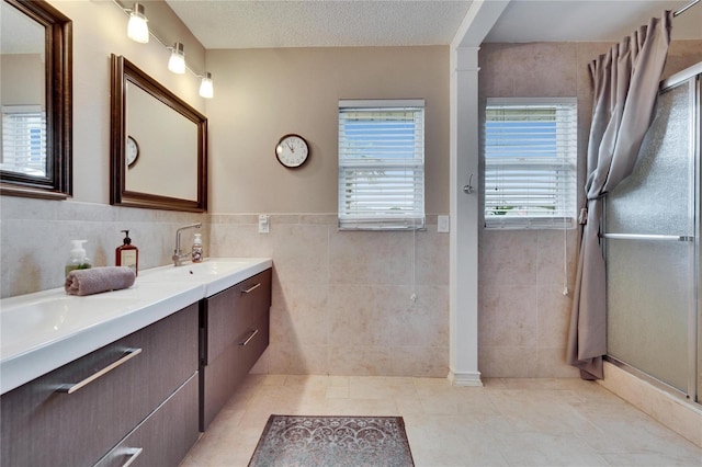 bathroom featuring tile walls, double vanity, a sink, a textured ceiling, and tile patterned floors