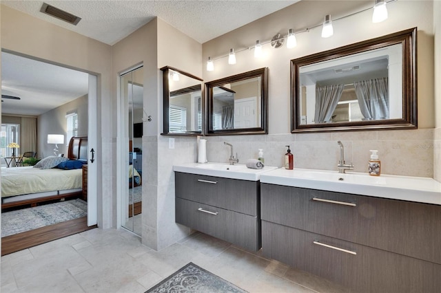 full bath with a sink, a textured ceiling, tile walls, and connected bathroom