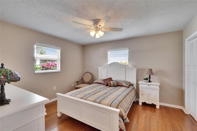 bedroom with a textured ceiling, multiple windows, baseboards, and wood finished floors