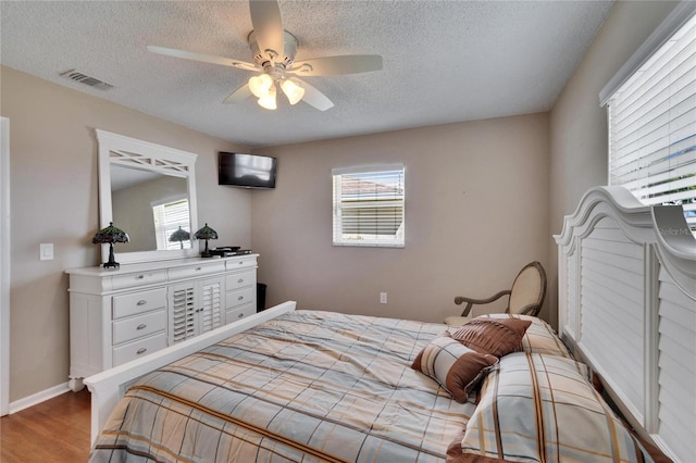 bedroom featuring a textured ceiling, multiple windows, light wood-type flooring, and visible vents