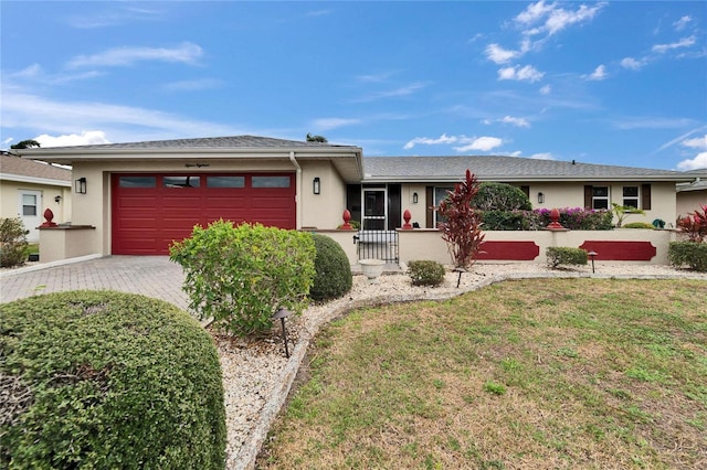 ranch-style home featuring a front lawn, decorative driveway, an attached garage, and stucco siding