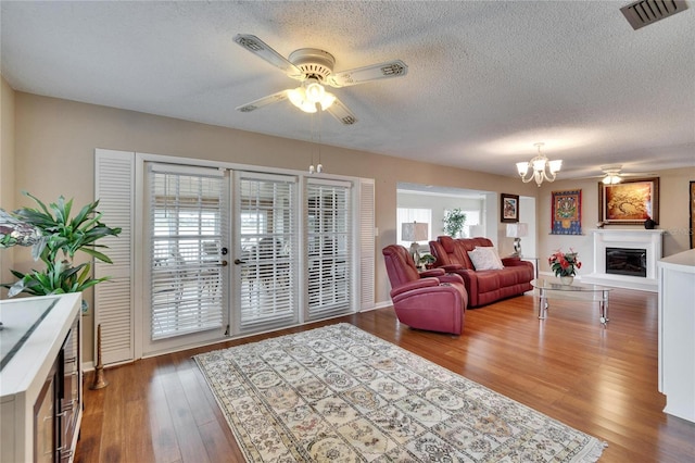 living room with a textured ceiling, ceiling fan with notable chandelier, wood finished floors, visible vents, and a glass covered fireplace