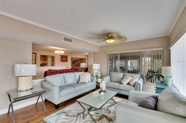 living room with a textured ceiling, ceiling fan with notable chandelier, wood finished floors, visible vents, and ornamental molding