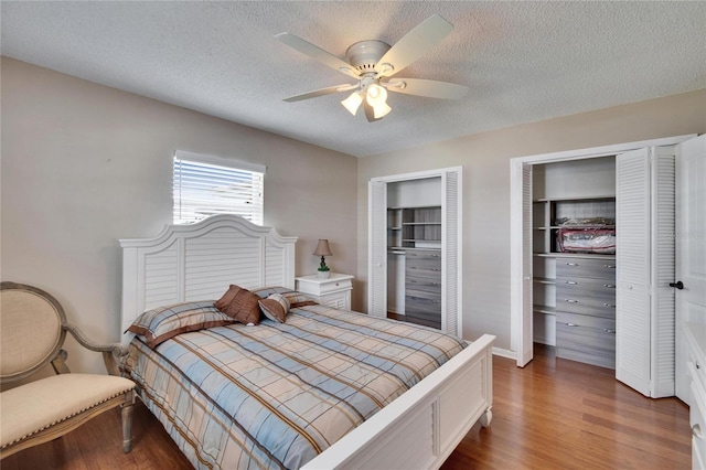 bedroom with a ceiling fan, dark wood-style flooring, a textured ceiling, and two closets