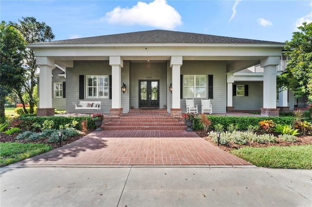 view of exterior entry with covered porch, roof with shingles, and french doors