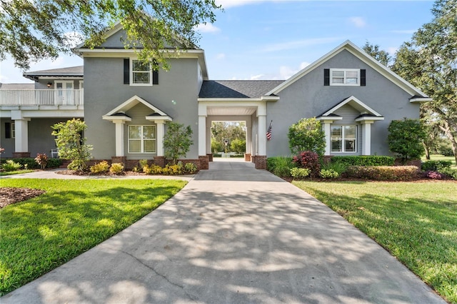 view of front of home featuring driveway, a balcony, a front lawn, and stucco siding