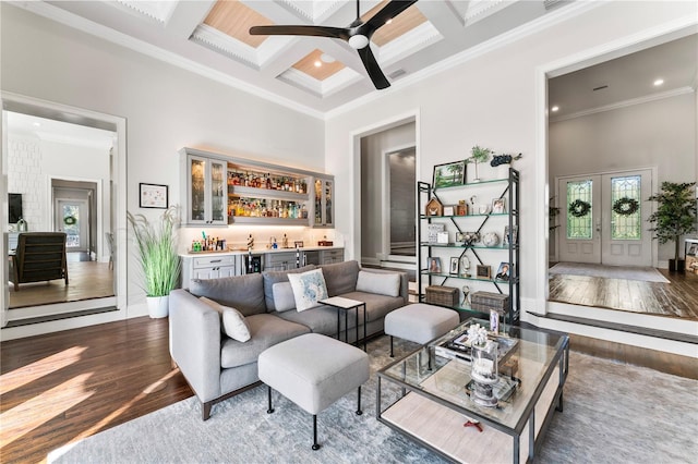 living area featuring coffered ceiling, a towering ceiling, wood finished floors, crown molding, and indoor wet bar