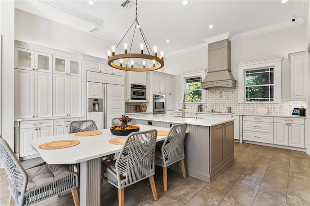 kitchen featuring oven, a sink, custom exhaust hood, tasteful backsplash, and a large island with sink