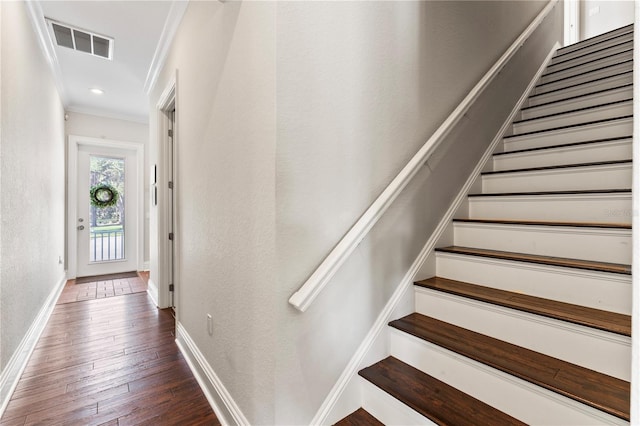 staircase featuring a textured wall, hardwood / wood-style flooring, visible vents, baseboards, and ornamental molding