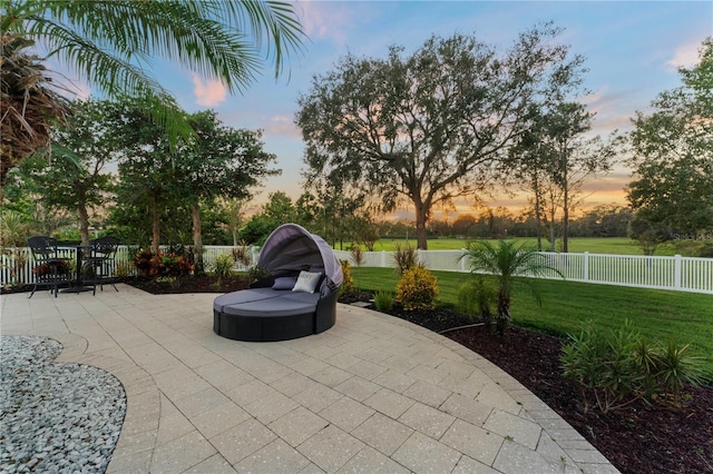 patio terrace at dusk featuring fence and a lawn