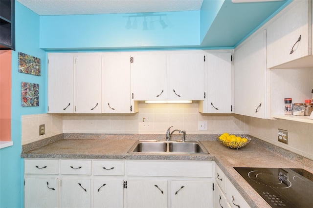 kitchen with black electric stovetop, tasteful backsplash, light countertops, white cabinetry, and a sink