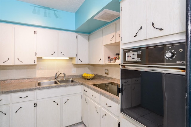 kitchen with wall oven, light countertops, white cabinetry, and a sink