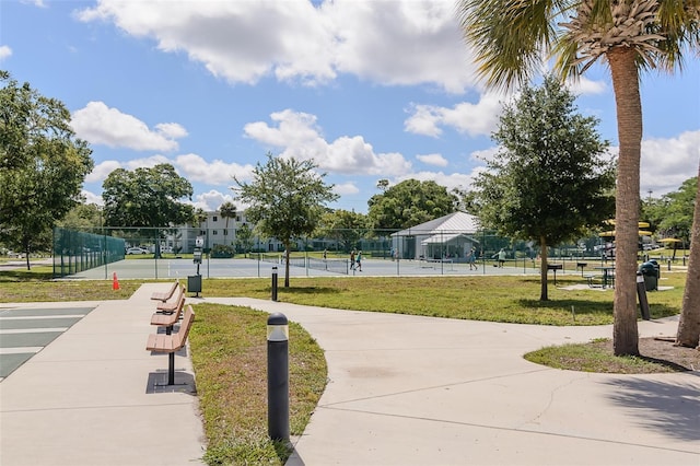 view of community with a yard, a tennis court, and fence