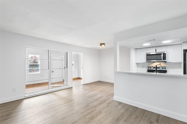 unfurnished living room featuring visible vents, light wood-style flooring, and baseboards