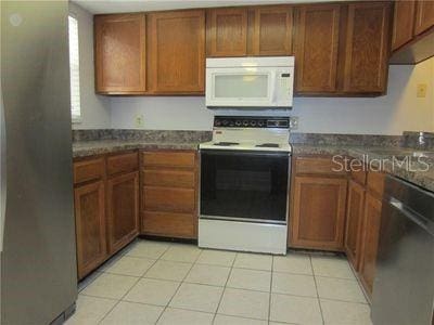 kitchen with electric range oven, white microwave, stainless steel dishwasher, and brown cabinets