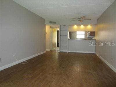 unfurnished living room with visible vents, dark wood finished floors, baseboards, and ceiling fan