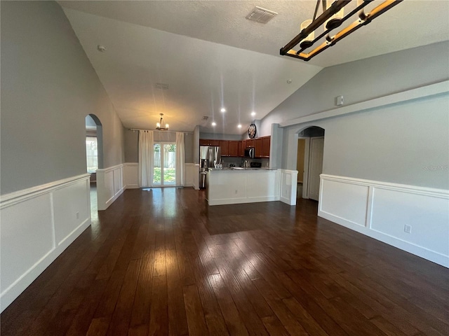 unfurnished living room with arched walkways, a chandelier, lofted ceiling, dark wood-type flooring, and wainscoting