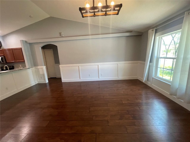 unfurnished dining area with lofted ceiling, arched walkways, dark wood-style floors, a chandelier, and a wainscoted wall