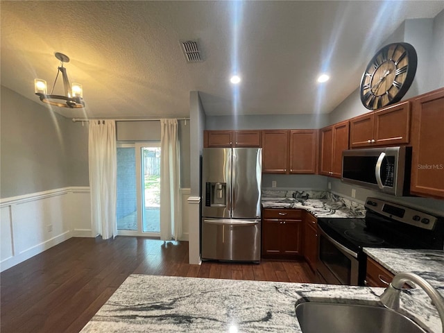 kitchen with appliances with stainless steel finishes, a sink, dark wood-style flooring, light stone counters, and wainscoting