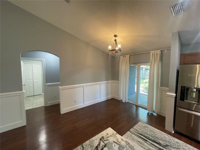 unfurnished dining area featuring arched walkways, dark wood-style floors, a chandelier, wainscoting, and a textured ceiling