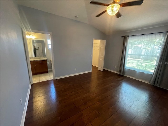 unfurnished bedroom with hardwood / wood-style floors, lofted ceiling, baseboards, ensuite bath, and ceiling fan