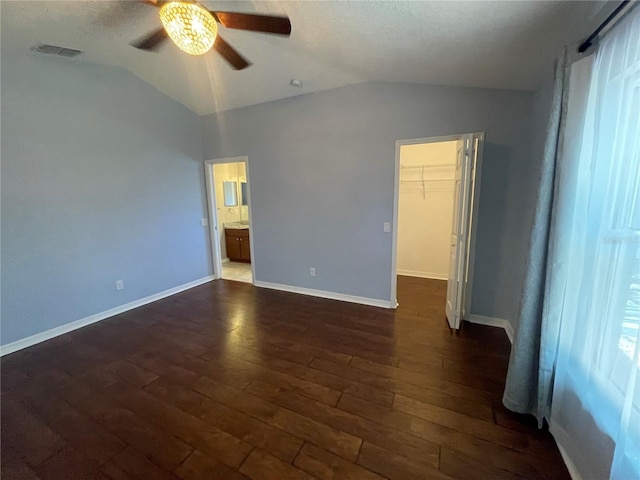 unfurnished bedroom featuring lofted ceiling, dark wood-style floors, a spacious closet, ceiling fan, and baseboards