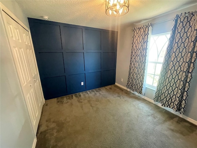 carpeted spare room featuring baseboards, a textured ceiling, a chandelier, a smoke detector, and a decorative wall