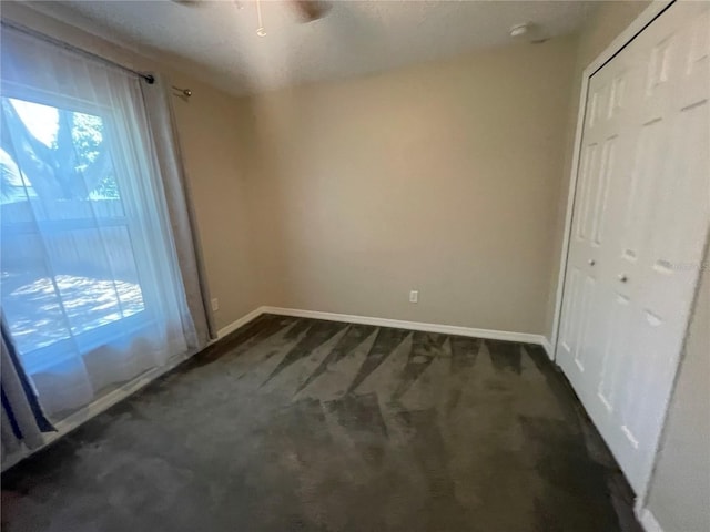 unfurnished bedroom with dark carpet, baseboards, a closet, and ceiling fan