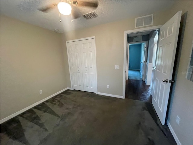 unfurnished bedroom with baseboards, dark colored carpet, a closet, and a ceiling fan