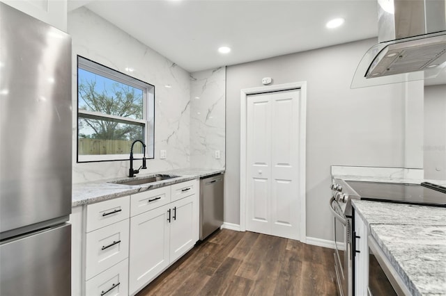 kitchen featuring island exhaust hood, appliances with stainless steel finishes, white cabinets, a sink, and light stone countertops