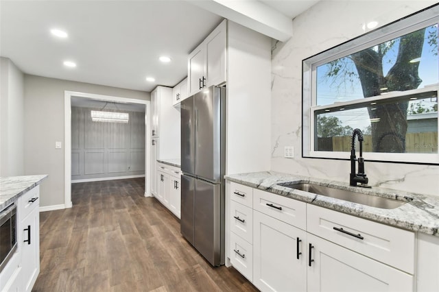 kitchen featuring light stone counters, a sink, freestanding refrigerator, and white cabinetry