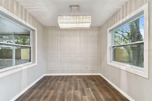 spare room featuring dark wood-style floors, baseboards, and a chandelier