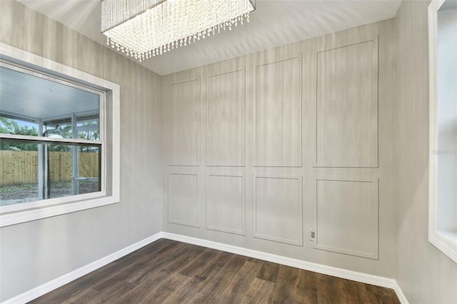 empty room featuring a notable chandelier, dark wood finished floors, and baseboards