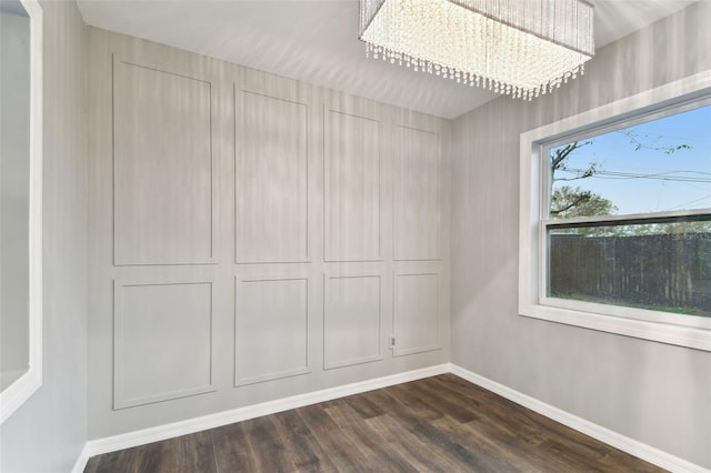 unfurnished room featuring dark wood finished floors, baseboards, and an inviting chandelier