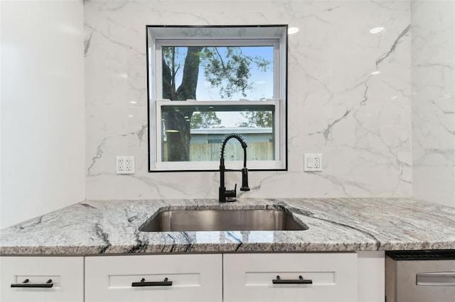 kitchen with a sink, light stone countertops, and white cabinets