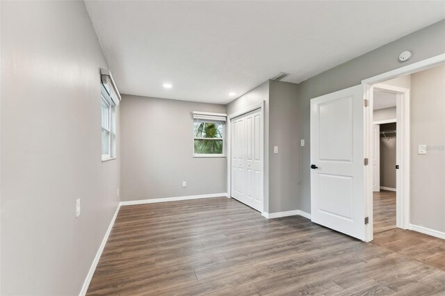 unfurnished bedroom with recessed lighting, a closet, baseboards, and wood finished floors