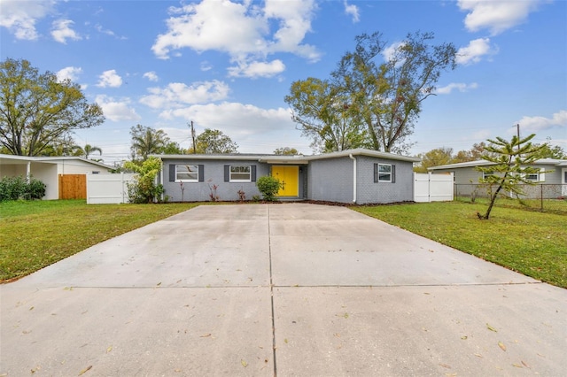 view of front facade with driveway, brick siding, a front yard, and fence