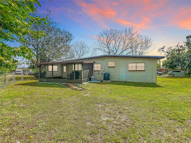 back of house with a sunroom, fence, a lawn, and central AC