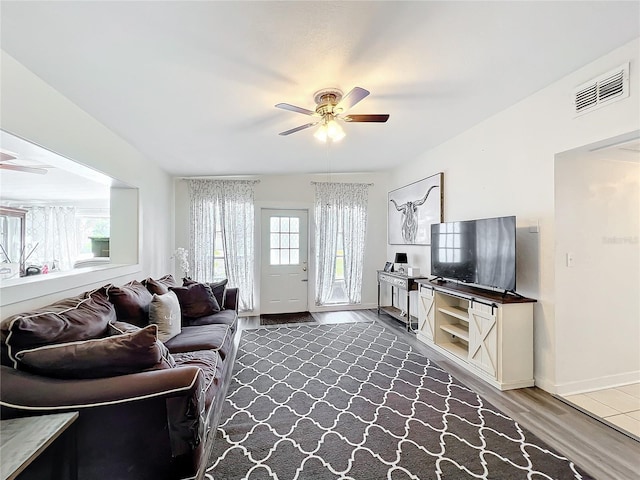 living room with a ceiling fan, visible vents, baseboards, and wood finished floors