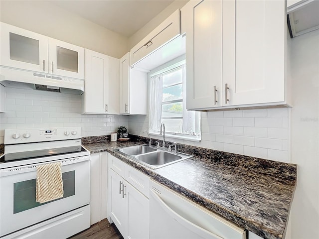 kitchen featuring white appliances, white cabinets, dark countertops, under cabinet range hood, and a sink