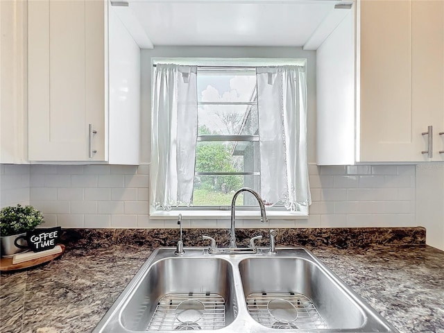 kitchen with tasteful backsplash, white cabinetry, a sink, and dark stone countertops