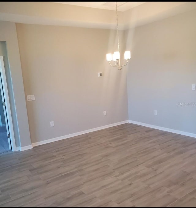 unfurnished room featuring a chandelier, baseboards, and wood finished floors