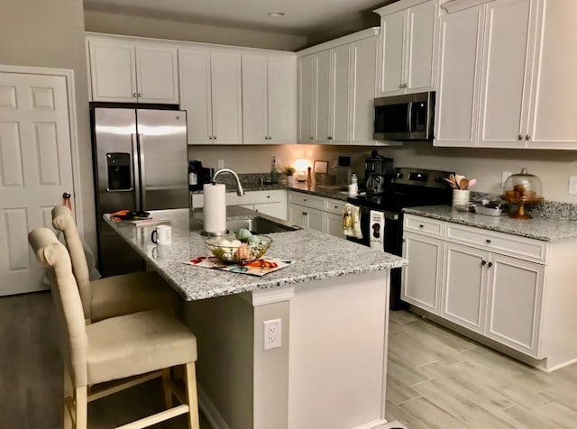 kitchen featuring light stone counters, stainless steel appliances, a kitchen bar, white cabinetry, and a sink