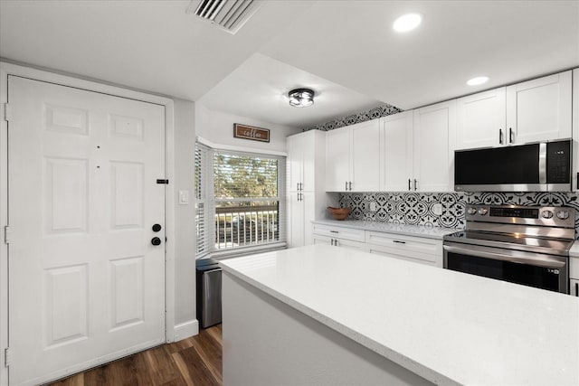 kitchen with tasteful backsplash, white cabinets, dark wood-style floors, stainless steel appliances, and light countertops