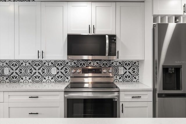 kitchen featuring appliances with stainless steel finishes, white cabinets, light stone counters, and tasteful backsplash