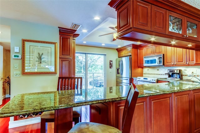 kitchen with stainless steel appliances, visible vents, backsplash, a sink, and dark stone countertops