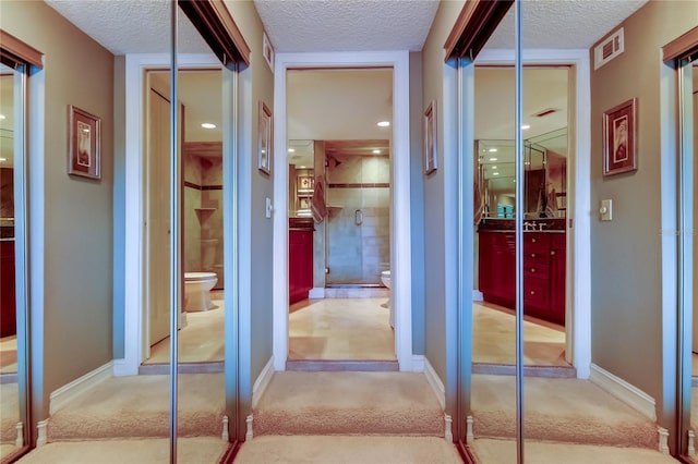 hall with carpet, visible vents, and a textured ceiling