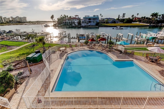 community pool featuring a patio area, a water view, fence, and a boat dock